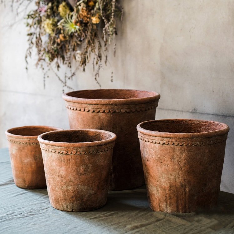 Set of four Large Terracotta Red Concrete Planters in varying sizes with aged rustic finish and scalloped rim detail, styled on a stone surface with dried botanicals in the background